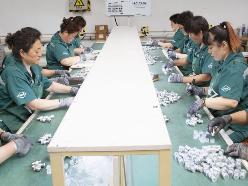 Several workers are assembling fluid connectors with plastic cap.